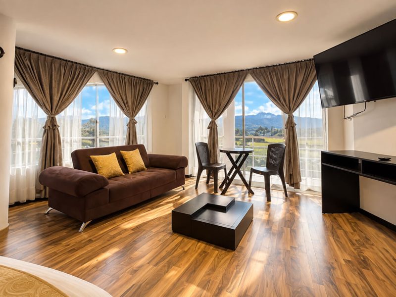 Sala de una suite con sofá, comedor y ventanales