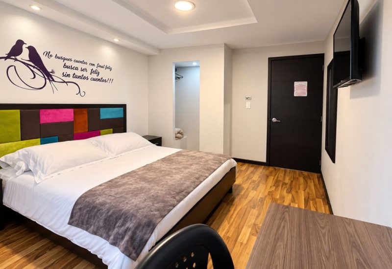 Cama doble con cabecero de colores y frase decorativa en la pared