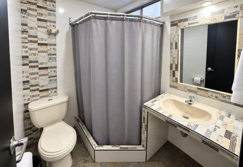 Baño con ducha de cortina gris, lavamanos y sanitario