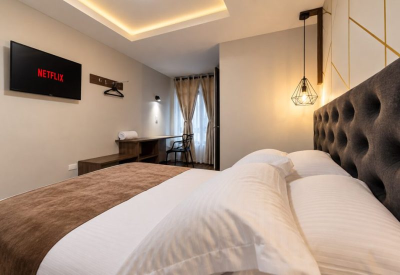 Cama con cabecero acolchado, lámpara colgante y televisor