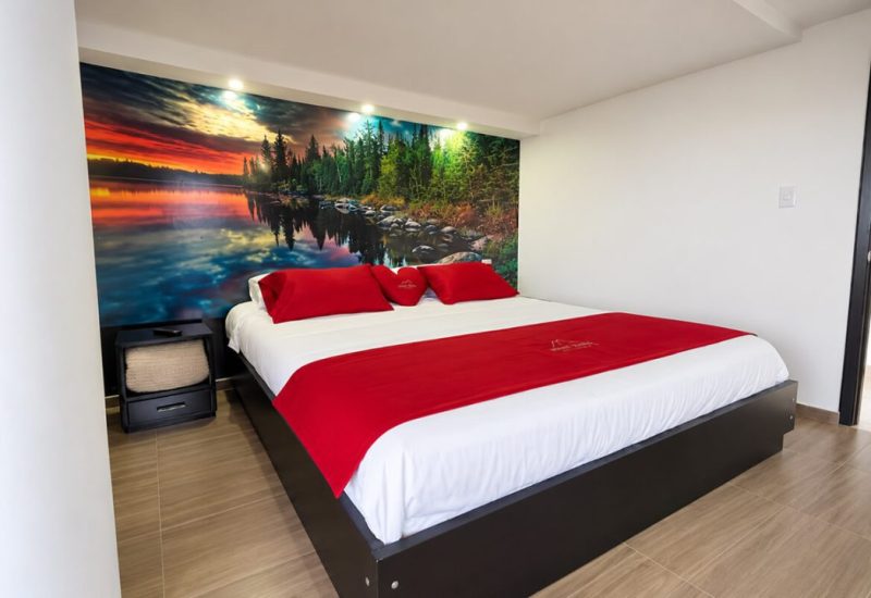 Cama king con cojines rojos y mural de lago al atardecer