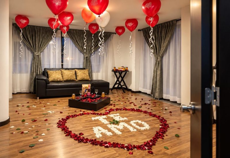Sala de una suite decorada con globos y la frase «Te amo» en pétalos