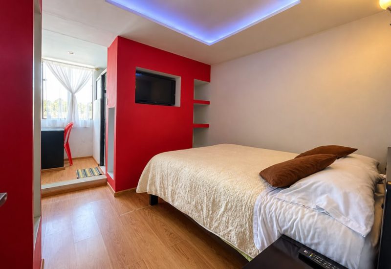 Habitación con cama doble, pared roja y luz en el techo