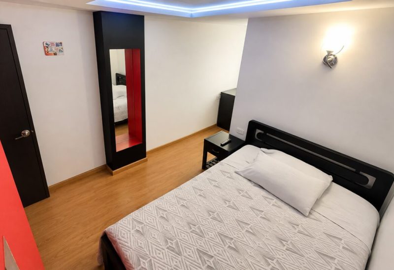 Habitación con cama doble, piso de madera y pared roja