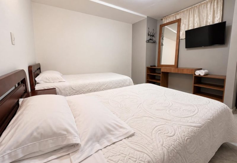 Habitación con dos camas tendidas en blanco y televisor